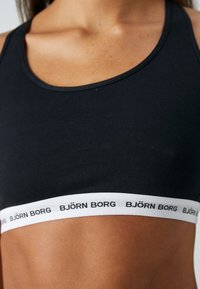 Čierna bezšvová športová podprsenka s bielym elastickým pásom s textom "BJÖRN BORG". Hladká tkanina s priliehavým strihom, okrúhlym výstrihom a úzkymi ramienkami.