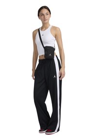 Svarta joggartights med en vit sidstripe, parat med en vit linne och en liten svart crossbody-väska med logotyp. Skor med röda detaljer.