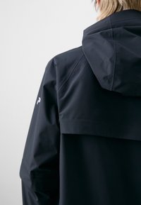 Black waterproof jacket features a hood, textured fabric, and a distinct shoulder panel. Has a small white logo on the sleeve.