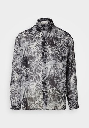 Chemise à boutons en motif abstrait noir et blanc. Caractérisée par un col classique, des manches longues et une texture de tissu léger et transparent.