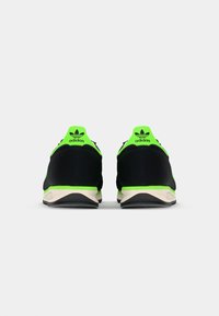 Black athletic shoes with a neon green accent on the heel and logo, featuring a textured upper and a contrasting cream sole.