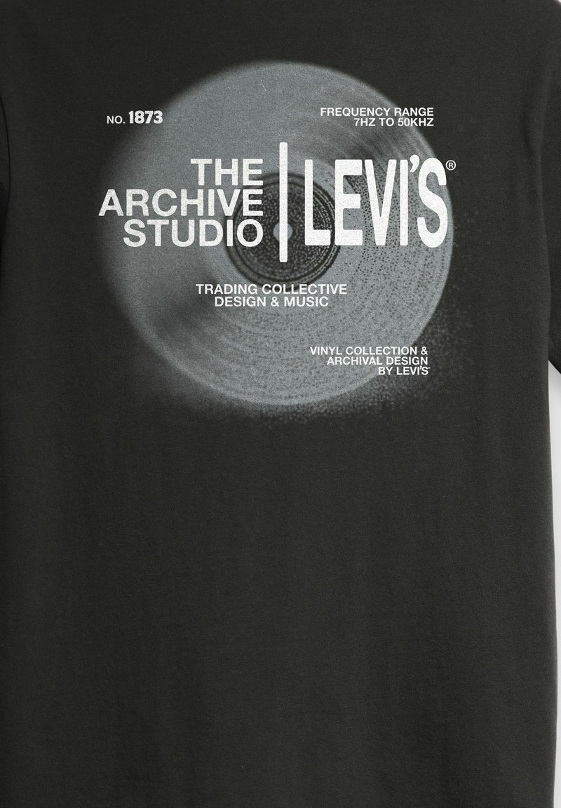 Chemise noire avec un texte blanc présentant un design de disque vinyle et des phrases sur The Archive Studio, Levi's, et la plage de fréquences musicales de 7Hz à 50kHz.