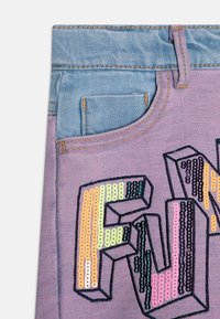 Lila tyg närbild med en stor, broderad "FUN" i flerfärgade paljetter. Ovan har en blå denimmidja med synlig sömnad.
