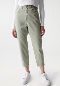 Světle zelené vysoké džíny s rovnými nohavicemi, designem pěti kapes a zapínáním na knoflík, doplněné bílými teniskami.