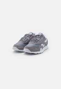 Graue Wildleder- und Leder-Sneaker mit weißen Akzenten, runder Spitze und strukturiertem Gummisohle. Mit Schnürsenkeln und einem Markenetikett auf der Zunge.