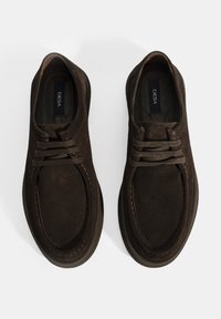 Chaussures en suede marron avec une forme arrondie, dotées d'un laçage à l'avant, de coutures contrastées et d'une semelle texturée. Étiquette de marque à l'intérieur.