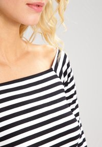 Haut rayé noir et blanc avec un décolleté carré, des manches longues et une texture douce, mettant en valeur de larges lignes horizontales.