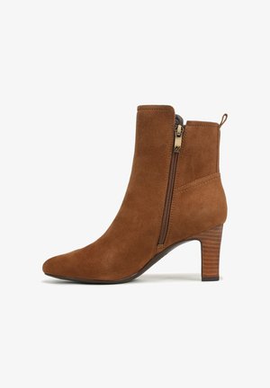 Stivaletto in suede marrone con punta affusolata, dettaglio della cerniera dorata e tacco impilato. Presenta una linguetta sul retro per facilitare l'indossamento.