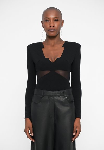 Bodysuit noir à manches longues et décolleté en V profond, avec des panneaux en mesh à la taille. Assorti avec un pantalon en cuir noir taille haute.