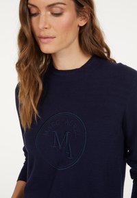 Navy blue sweatshirt featuring an embossed circular logo with the text "MARC AUREL" and "MA." Made from soft fabric with a crew neckline.