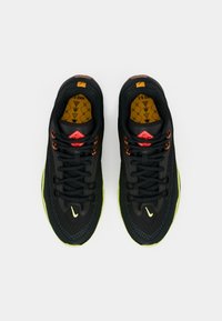 Ζευγάρι μαύρων και φωσφοριζέ κίτρινων αθλητικών παπουτσιών Nike, ορατό από πάνω σε λευκό φόντο, με υφή από δίχτυ και κορδόνια.