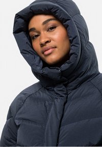 Navyblauer gepolsterter Jacke mit einer auffälligen, übergroßen Kapuze, mit gestepptem Muster und einem Frontreißverschluss. Weicher, leichter Stoff.