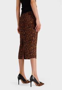 Gonna a tubino in stampa leopardata con spacchi laterali, realizzata in tessuto testurizzato. Scarpe nere con tacco alto, dalla punta affusolata e con dettagli a fiocco.