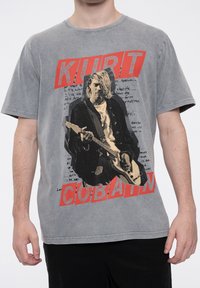 Gray cotton t-shirt featuring a graphic of a musician, with "KURT" and "COBAIN" in bold red text above and below. Textured, casual fit.