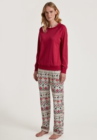 Red long-sleeve top with crew neck and ribbed cuffs paired with patterned pants featuring a geometric design in red, blue, and cream.