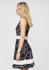 Robe géométrique noir et blanc avec un corsage ajusté, une large ceinture blanche et une jupe évasée. Tissu lisse avec un léger éclat.