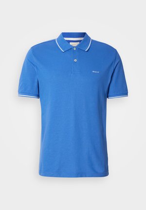 Blå polo-shirt laget av bomull med klassisk krage. Har hvit kanting på ermene, logo på brystet og knappestolpe.