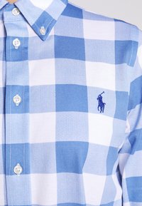 Sinivalkoruudullinen nappipaita, jossa kaulus ja kirjailtu logo, jossa on polopelaaja ratsun selässä rinnassa.