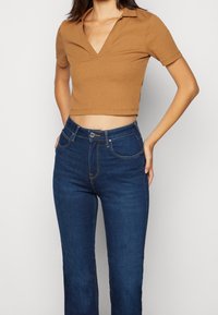 Brun bomull kortärmad polo med V-hals; kombinerad med mörkblå denim jeans med utsvängd modell som har framfickor och en midjebutton.