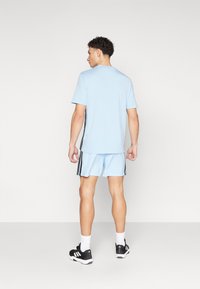 Šviesiai mėlynas sportinis marškinėliai ir šortai su juodomis šoninėmis juostelėmis, derinami su juodais sportiniais batais. Matomi siūlės ir trumpi rankoviai.