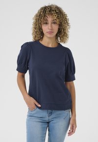 Navy blue cotton t-shirt with puffed short sleeves, round neckline, and a relaxed fit, paired with light blue jeans. Smooth texture and simple design.