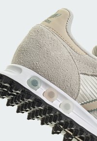 Μπέζ σουέτ αθλητικό παπούτσι με λευκή καουτσούκ σόλα, υφασμάτινα πάνελ και πολύχρωμες λεπτομέρειες στην επένδυση· διαθέτει υφή και ξεχωριστό σχέδιο.