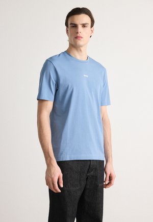 Helles blaues Baumwoll-T-Shirt mit kurzen Ärmeln und Rundhalsausschnitt. Mit einem kleinen weißen "BOSS"-Logo auf der Brust. Getragen mit dunklen Jeans.