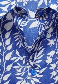 Blue linen shirt featuring white floral pattern. Notable details include a button with a blue accent and a classic collar design.
