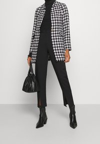 Blazer pied-de-poule noir et blanc, associé à un pantalon taille haute noir avec des fentes latérales, et un sac à cordon noir. Bottines noires.