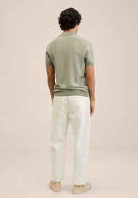 Polo à manches courtes vert clair avec col côtelé, associé à un pantalon blanc droit et des chaussures beige, vu de dos.