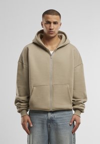 Beige zip-up hoodie gemaakt van een zachte katoenmix, met een grote capuchon, frontzakken en losvallende lange mouwen.