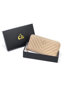 Beżowy pikowany portfel z suwakiem, z małym akcentem w postaci ważki, zaprezentowany w czarnym pudełku z złotym logo. Teksturowany materiał syntetyczny.