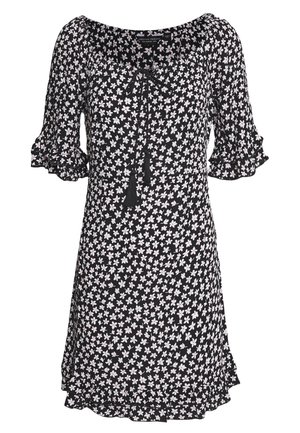 Robe noire à motif floral blanc, manches mi-longues avec volants, encolure en U et détail de nœud à l'avant avec des pompons.