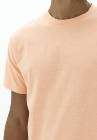 T-shirt à manches courtes de couleur pêche, en doux mélange de coton, col rond, texture subtile et design simple sans motifs ni embellissements visibles.
