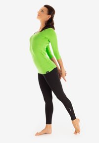 Grøn, langærmet atletisk top med en scooped halsudskæring, parret med sorte leggings. Outfittet sidder tæt til kroppen og har en glat tekstur.
