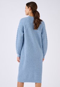 Abito di maglia azzurro chiaro con dettagli a trecce sulle spalle e sulle maniche, caratterizzato da una linea diritta e polsini a coste. Morbido al tatto.