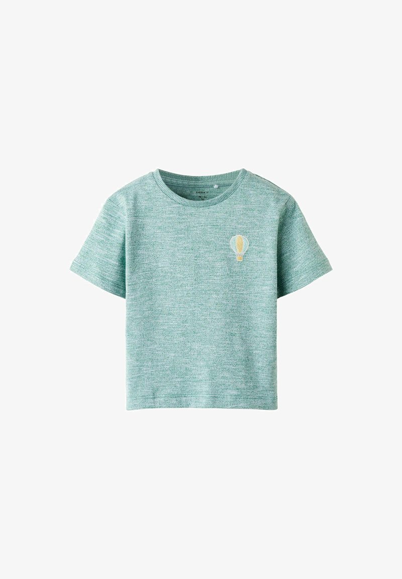 Camiseta corta de mangas en verde claro, con un patrón texturizado y un pequeño detalle bordado de un globo aerostático en el pecho.