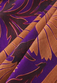 Colorful fabric featuring purple and brown tones with large, abstract leaf patterns and intricate details in red and orange. Smooth texture.