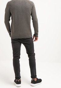 Pull en tricot gris avec un col rond, des poignets et un ourlet côtelés, associé à un jean slim noir et des baskets noires. Tenue décontractée vue de dos.