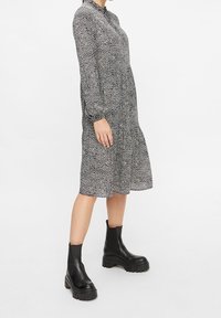 Vestido midi de lunares en blanco y negro con mangas largas, cuello alto y corte holgado, combinado con botas de tobillo negras y gruesas.