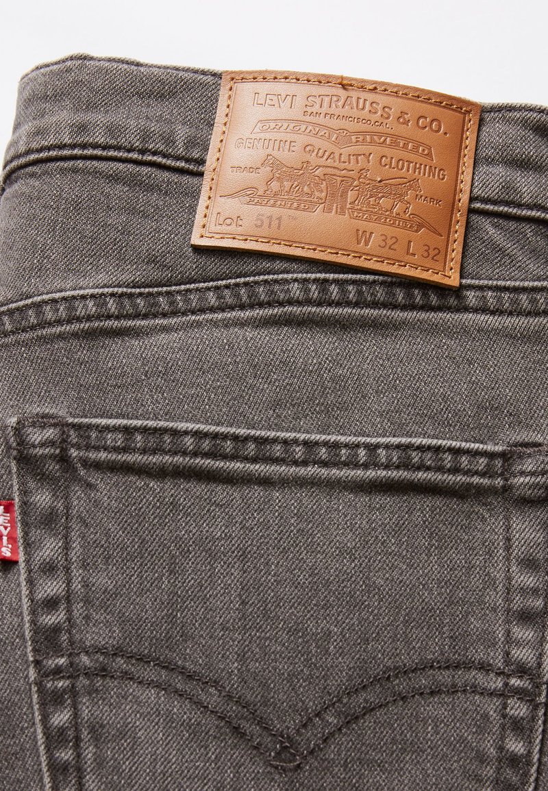 Jeans en denim gris avec une étiquette en cuir portant l'inscription "Levi Strauss & Co." avec un texte en relief et des détails de taille. Étiquette rouge sur la poche arrière.