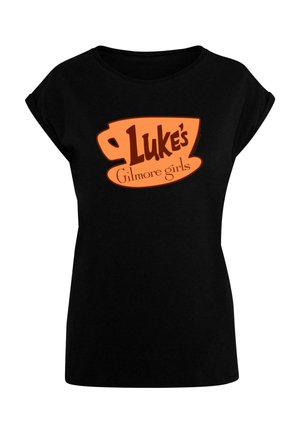 T-shirt noir à manches courtes avec un graphisme d'une tasse orange portant le texte "Luke's" et "Gilmore girls" en typographie marron. Coupe classique.