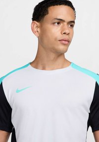 Camiseta de Nike con un cuerpo blanco, mangas negras y acentos en aqua en los hombros y en el logotipo. Textura suave con un cuello redondo.