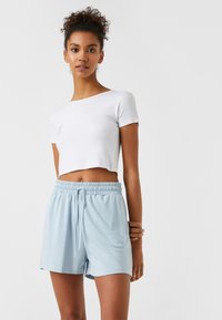 Camiseta corta blanca de manga corta, combinada con pantalones cortos de cintura elástica color azul claro con cordón. Textura de tela suave.