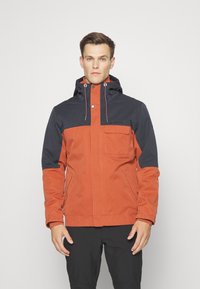 Giacca impermeabile arancione e blu navy, con zip frontale, cappuccio con cordini regolabili e tasca sul petto.