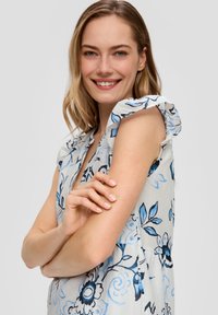 Blumenmusterkleid mit einer hellgrauen Basis und blauen sowie schwarzen Designs. Rüschensleeves und ein V-Ausschnitt sorgen für Struktur.
