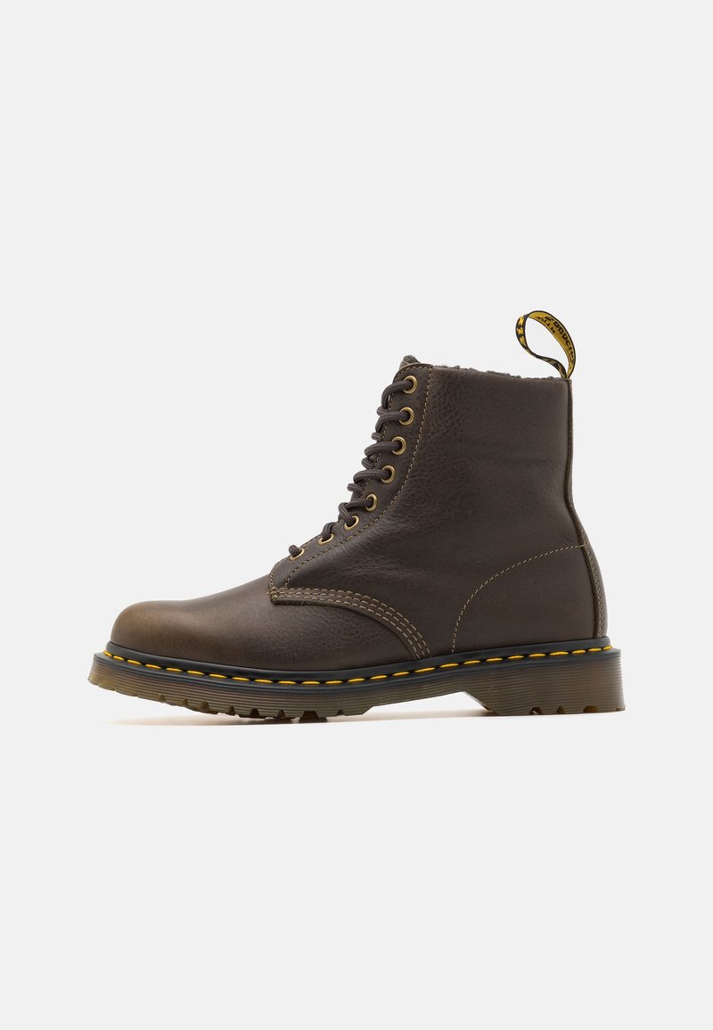 Botte en cuir marron foncé à lacets, couture jaune, languette au talon et semelle épaisse texturée sur fond uni.