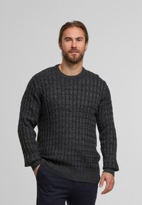 Grauer strukturierter Pullover mit einem Kabelstrickmuster, Rundhalsausschnitt und gerippten Bündchen und Saum. Über einer marineblauen Hose getragen.