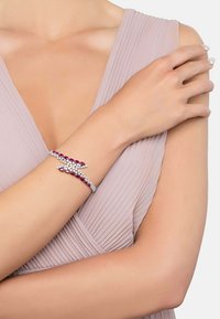 Silver and ruby bracelet with a twisting design, featuring clear gemstones along a flexible band, worn on a bare arm.