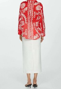Vrouw in een rood en wit gestreepte lange blouse, witte midi-rok en zwarte haksandalen, gezien vanuit de rug.